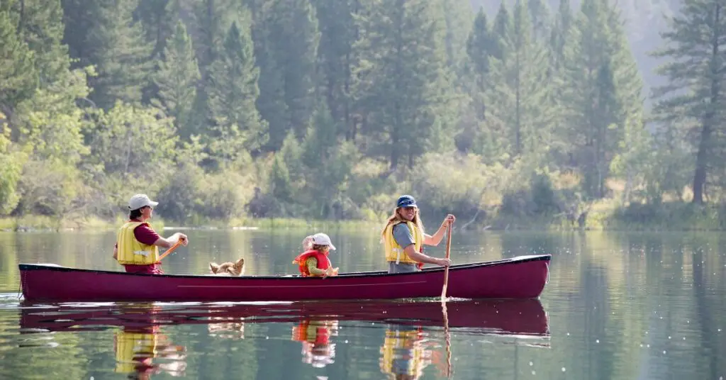 A family with a child paddling a red canoe on a calm lake, highlighting affordable travel in Canada using the Parks Canada Discovery Pass and Canada Strong Pass 2026.