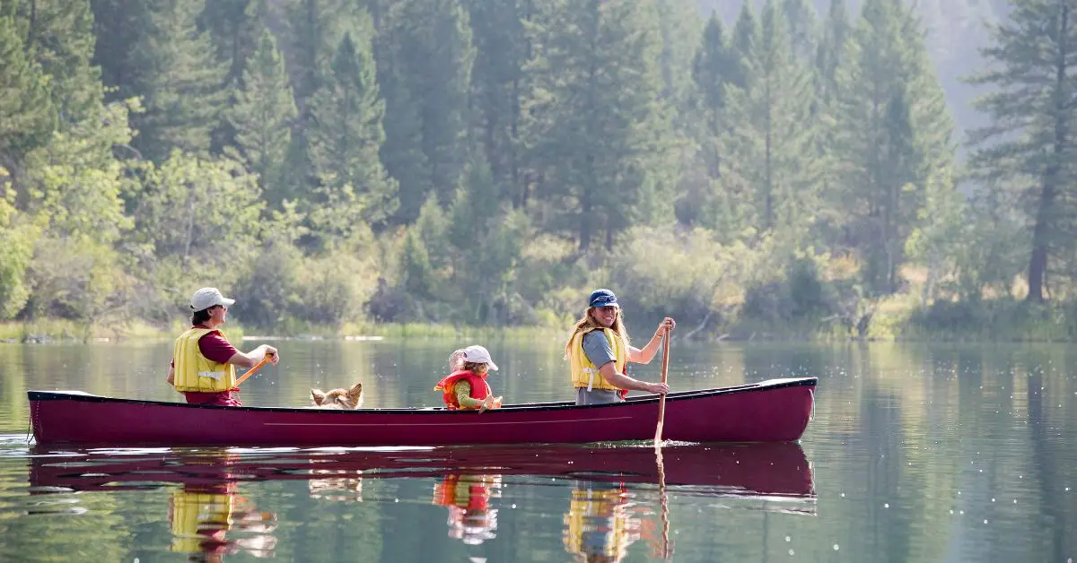 A family with a child paddling a red canoe on a calm lake, highlighting affordable travel in Canada using the Parks Canada Discovery Pass and Canada Strong Pass 2026.