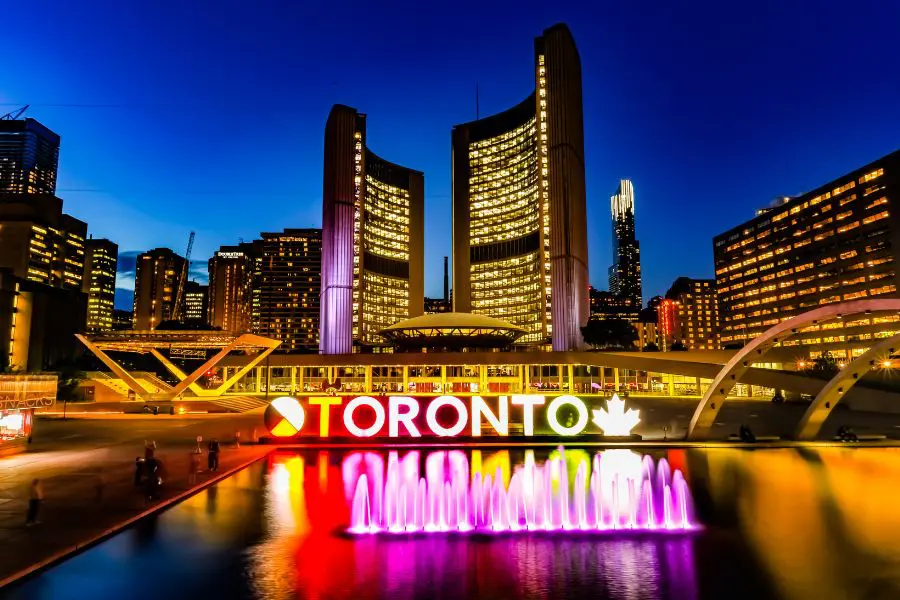 The vibrant, illuminated 3D Toronto sign glowing at night in front of City Hall at Nathan Phillips Square, welcoming newcomers.