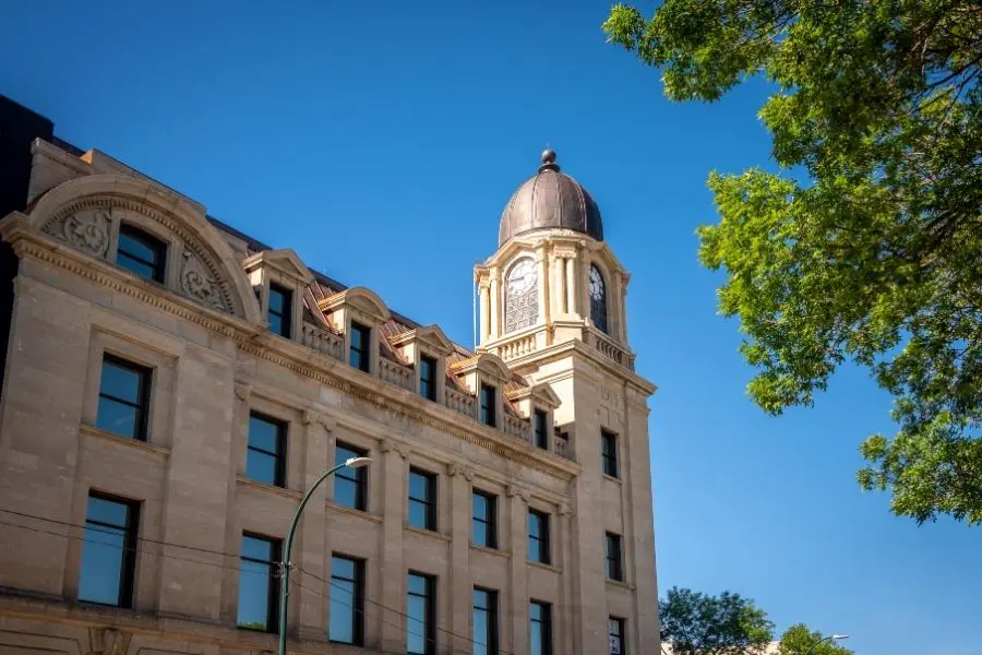 The historic limestone clock tower of the John D. Higinbotham Federal Building under a clear blue sky for newcomers living in Lethbridge, Alberta.