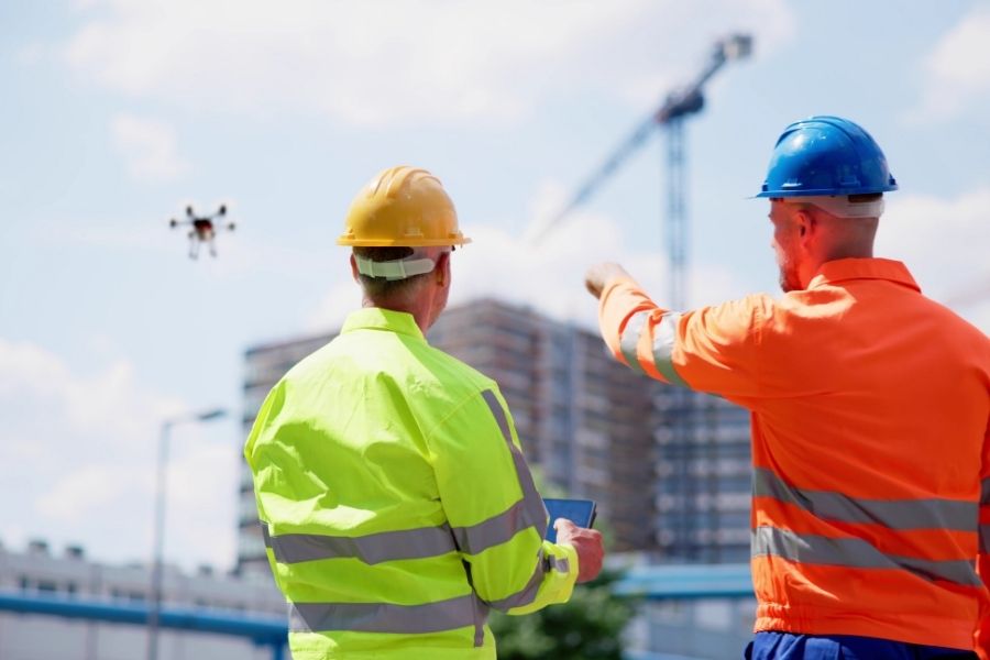Two construction workers using a drone and tablet to monitor a high-rise apartment project, illustrating the 2026 surge in housing supply in the Canada rental market.