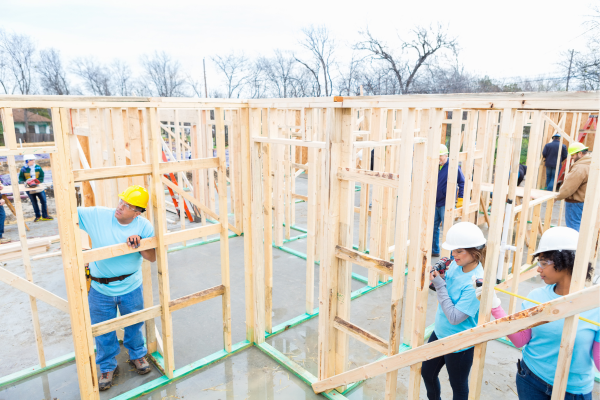 A team of volunteers wearing hard hats are building a home for a charitable organization.