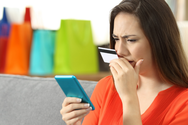 A woman is looking worried while looking at her credit card statement on her mobile phone. Avoiding credit card mistakes can help you build a good credit score in Canada.