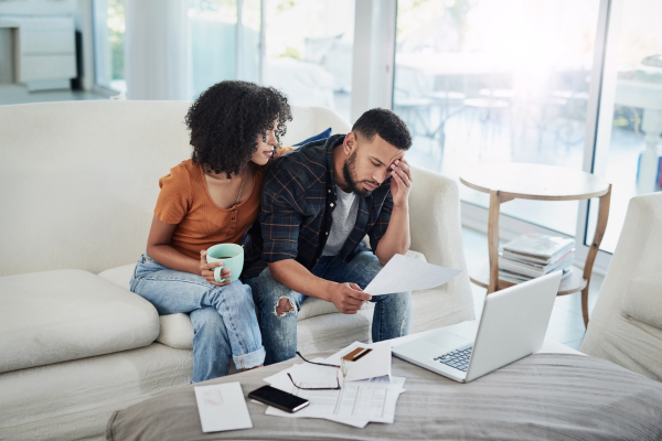 A concerned couple sits on a sofa to review bank statements that show they have reached their credit limit. Avoid this credit card mistake by spending within your means.