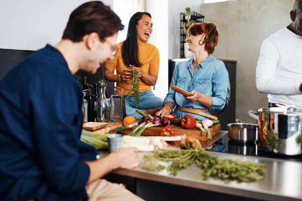 A homeowner shares a laugh with a housemate and friends as they prepare a meal together. 