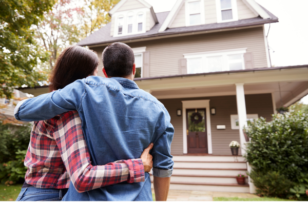 A young couple stands outside of a home they want to buy when interest rates in Canada move lower.