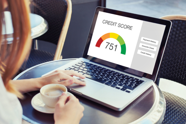 A woman drinks a coffee as she checks a credit score on a laptop. 