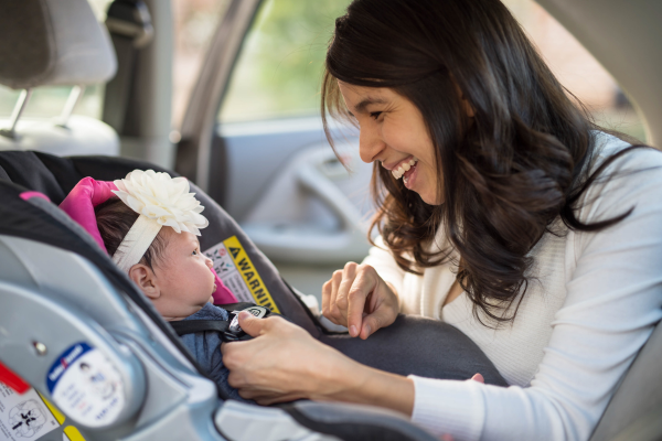 A woman carefully buckles and checks the straps on her newborn daughter's car seat before driving in Canada. 