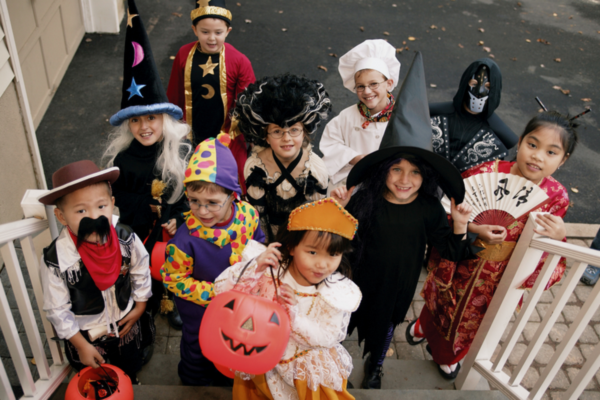 A group of young children are trick or treating and dressed in different costumes. 