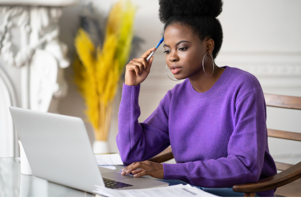 A woman is looking at a computer to research the housing market in Canada and the cost to buy a home.