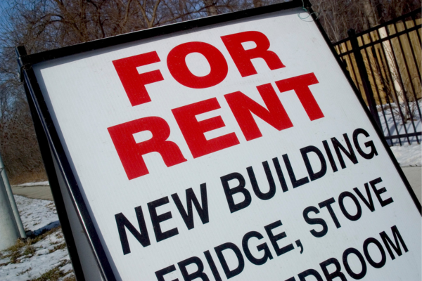 A sign advertising apartments for rent in Toronto sits on the sidewalk in front of a rental building. 