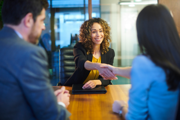 A young smiling woman job seeker shakes hands with another woman across a table as a man looks on. Canada's job market remained strong in November.