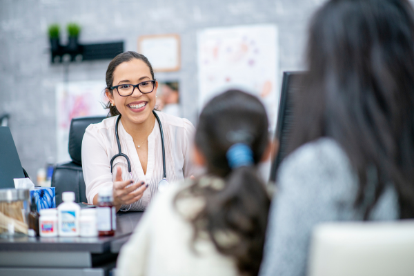 A female doctor is smiling and talking to a mother and her daughter  in the office. 