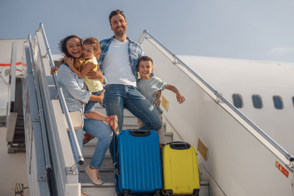 A young couple with children are smiling as the exit a plane. Newcomers can purchase travel medical health insurance before the arrive in Canada.