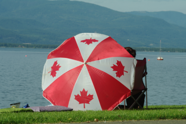 People relax at a beach while sitting under an oversized red and white umbrella on Canada Day.