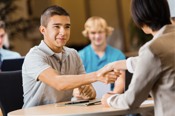 A young male teenager is smiling and shaking hands during an interview for a summer job in Canada