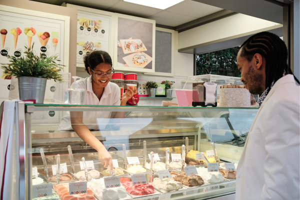 A young girl is serving ice cream to a customer from an ice cream fridge.