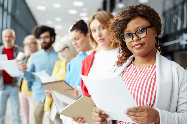 People are standing in line to prepare for interviews for jobs in Canada teaching. They have portfolios and samples of their work. 