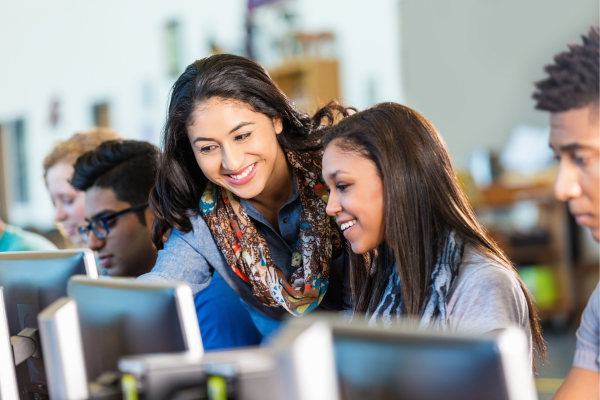 Secondary school teacher helping high school students with computers. The salary for Canada high school teaching jobs can vary.
