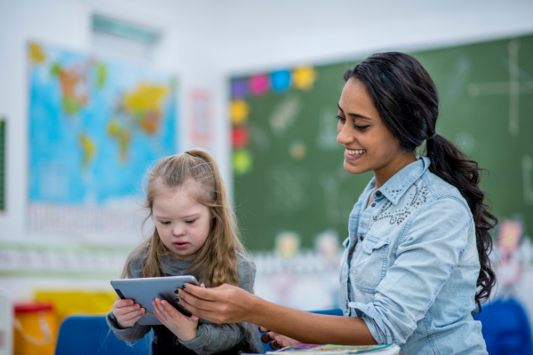 A female teacher is teaching technology to a young student using a tablet computer. 