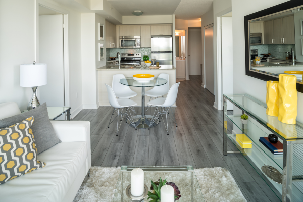 A white couch, glass eating table and a mirro above a long table form the main decor elements in a Toronto condo which are popular with newcomers