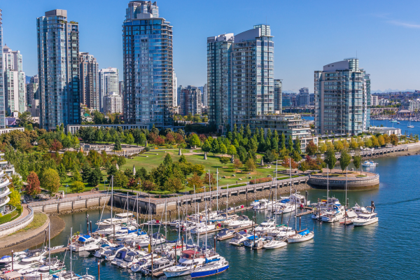 Docked sail boats rest adjacent to a tree-laden park and condo buildings in Vancouver