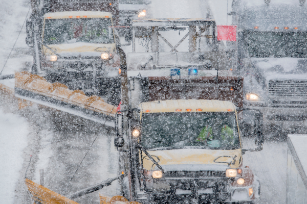 Two snow plows are clearing the road for vehicles in a storm.